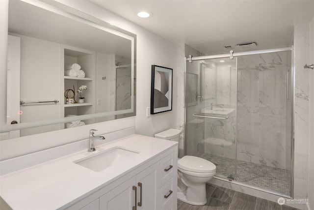 bathroom with vanity, a shower with shower door, toilet, and built in shelves