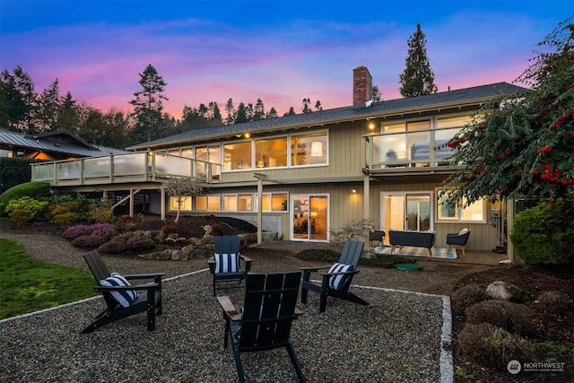 back house at dusk featuring a fire pit, a patio area, and a sunroom