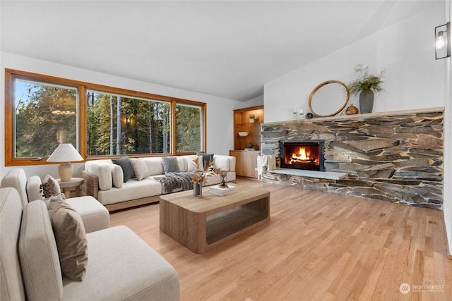 living room with a fireplace, vaulted ceiling, and light wood-type flooring