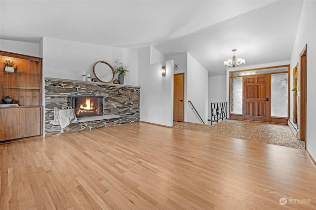 unfurnished living room with a baseboard heating unit, light hardwood / wood-style floors, a stone fireplace, vaulted ceiling, and a chandelier