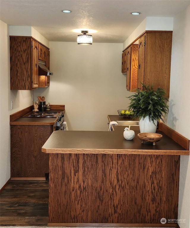 kitchen with dark wood-type flooring, kitchen peninsula, and a textured ceiling