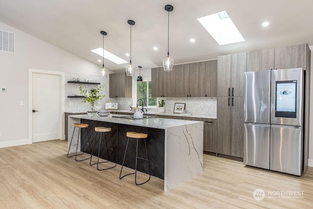 kitchen featuring stainless steel fridge, hanging light fixtures, light stone countertops, a center island, and decorative backsplash