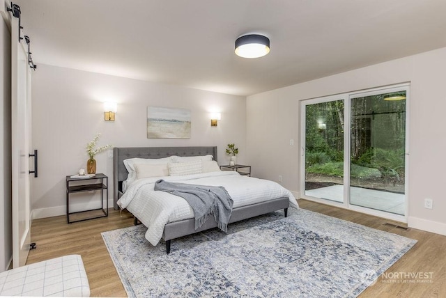 bedroom with access to outside, a barn door, and light wood-type flooring