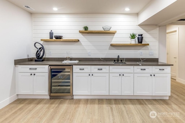 bar with white cabinets, beverage cooler, light hardwood / wood-style floors, sink, and backsplash