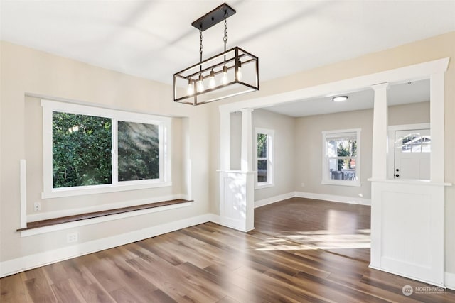 unfurnished dining area featuring dark wood-type flooring and decorative columns