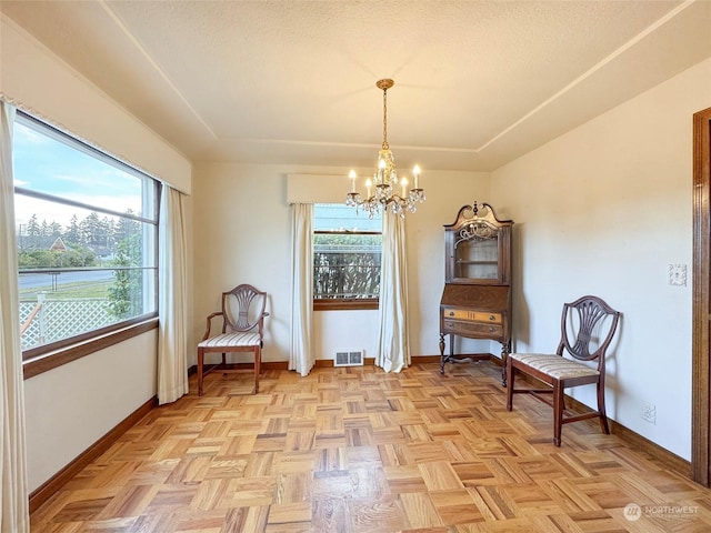 sitting room featuring light parquet floors, a healthy amount of sunlight, a textured ceiling, and an inviting chandelier