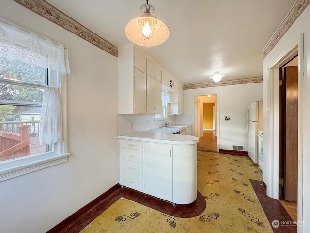 kitchen featuring white refrigerator, sink, white cabinets, and decorative light fixtures