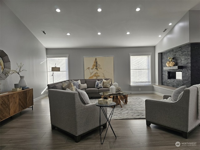 living room with a stone fireplace, dark wood-type flooring, and vaulted ceiling