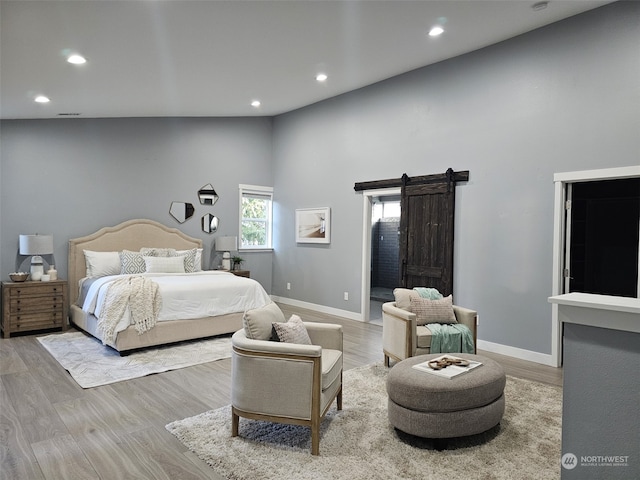 bedroom featuring a barn door, a high ceiling, and light wood-type flooring