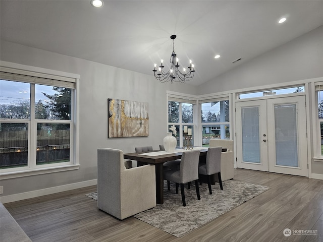 dining area with hardwood / wood-style floors, a notable chandelier, vaulted ceiling, and french doors