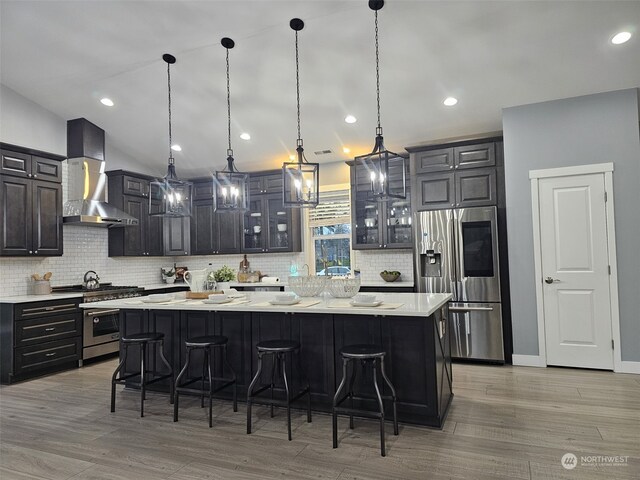 kitchen with a breakfast bar area, stainless steel appliances, a kitchen island, decorative light fixtures, and wall chimney exhaust hood