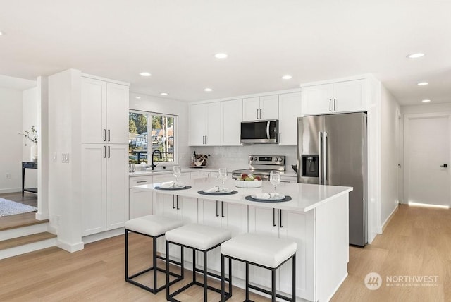 kitchen with white cabinetry, stainless steel appliances, a center island, and light hardwood / wood-style floors