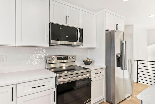 kitchen featuring appliances with stainless steel finishes, white cabinetry, decorative backsplash, light stone counters, and light hardwood / wood-style floors