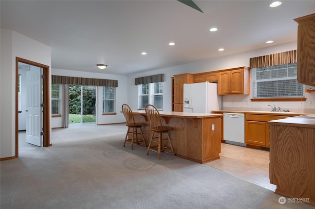 kitchen with a center island, white appliances, light carpet, and a breakfast bar