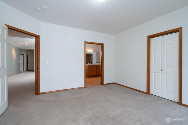 unfurnished bedroom with light colored carpet, a closet, and ensuite bath