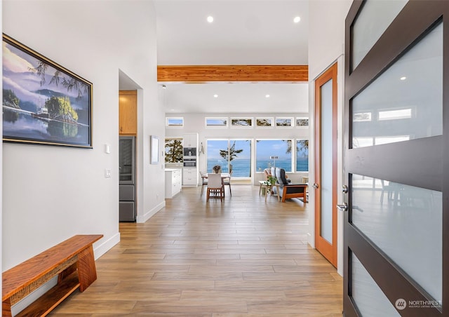 hallway with light hardwood / wood-style floors, beamed ceiling, and a water view