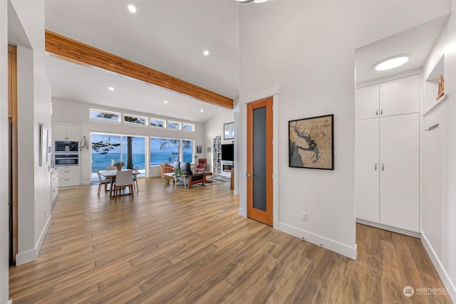 interior space with a towering ceiling, light hardwood / wood-style floors, and beamed ceiling