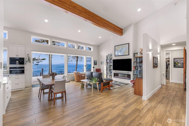 living room with beamed ceiling, a high ceiling, and light wood-type flooring