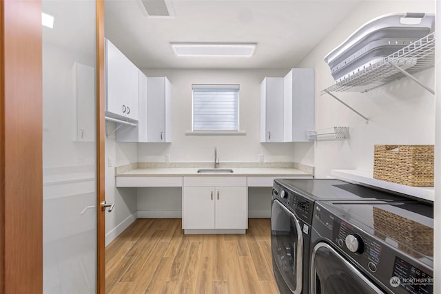 washroom with cabinets, washing machine and dryer, sink, and light hardwood / wood-style floors