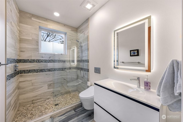 bathroom with tiled shower, vanity, and toilet