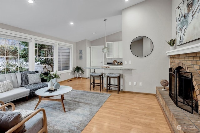 living room featuring a brick fireplace, high vaulted ceiling, and light hardwood / wood-style floors