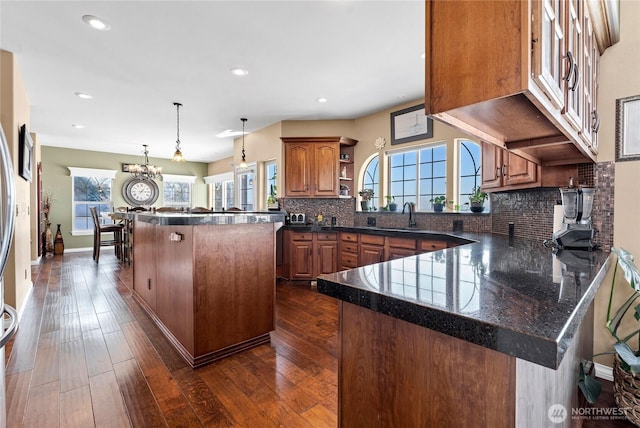 kitchen with hanging light fixtures, dark hardwood / wood-style floors, backsplash, and kitchen peninsula