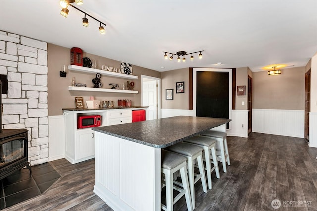 kitchen featuring dark hardwood / wood-style floors, a wood stove, white cabinets, a kitchen breakfast bar, and a center island