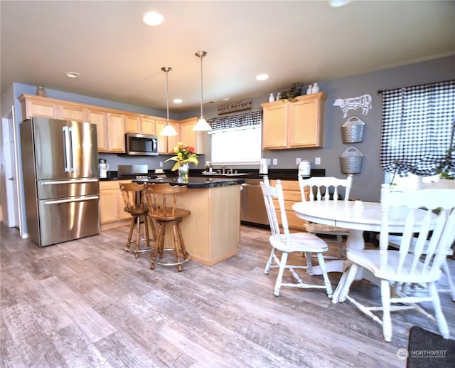 kitchen with a kitchen island, hanging light fixtures, stainless steel appliances, light brown cabinets, and light wood-type flooring