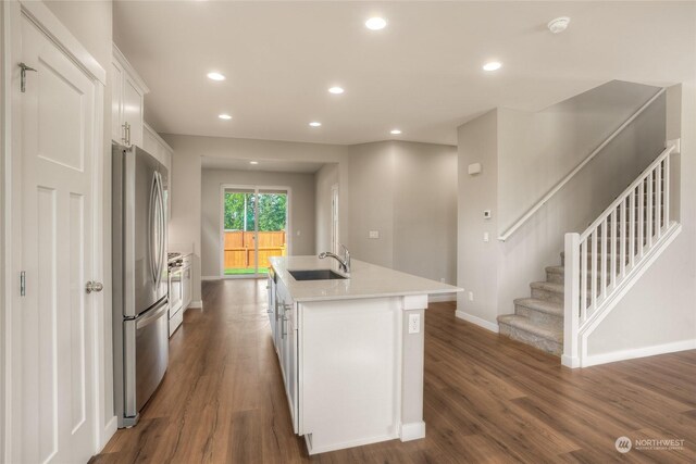 kitchen with sink, dark hardwood / wood-style floors, stainless steel fridge, an island with sink, and white cabinets