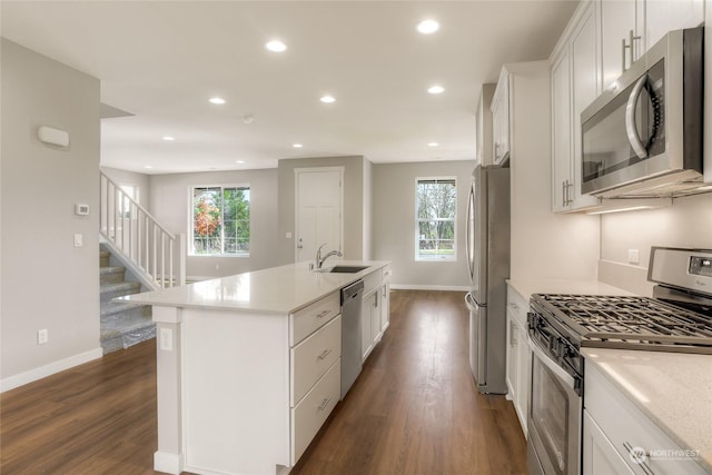 kitchen with appliances with stainless steel finishes, dark hardwood / wood-style floors, white cabinetry, an island with sink, and sink