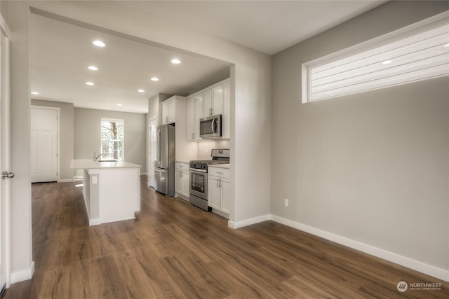 kitchen with appliances with stainless steel finishes, dark hardwood / wood-style floors, an island with sink, and white cabinets