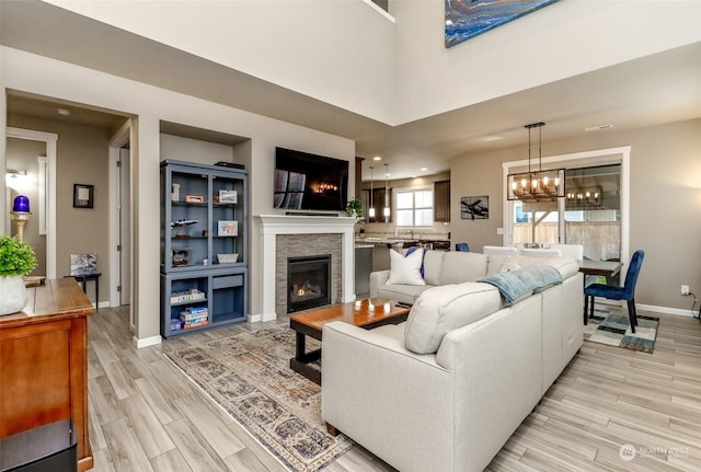 living room with a high ceiling, a stone fireplace, a notable chandelier, and light hardwood / wood-style flooring