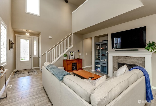 living room with a high ceiling, a stone fireplace, and light hardwood / wood-style flooring