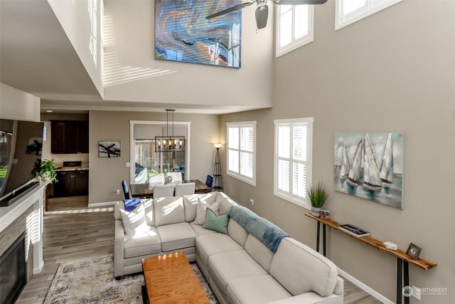 living room with a high ceiling, ceiling fan with notable chandelier, and light wood-type flooring