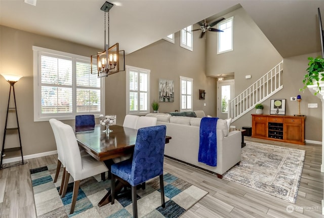 dining area with a towering ceiling, ceiling fan with notable chandelier, and light hardwood / wood-style floors