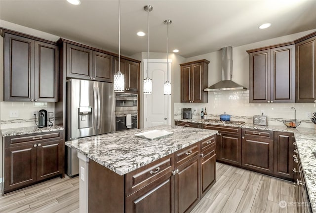 kitchen with appliances with stainless steel finishes, pendant lighting, tasteful backsplash, dark brown cabinetry, and wall chimney range hood