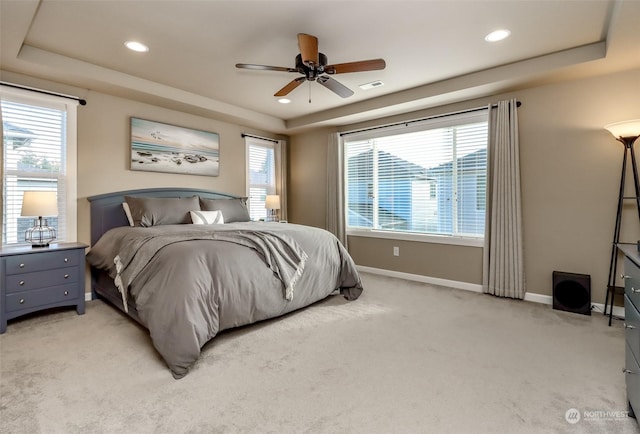 carpeted bedroom featuring multiple windows, ceiling fan, and a tray ceiling