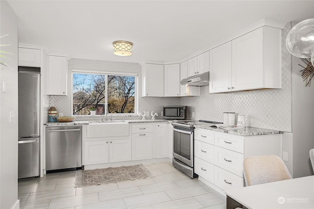 kitchen with appliances with stainless steel finishes, sink, white cabinets, decorative backsplash, and light stone counters