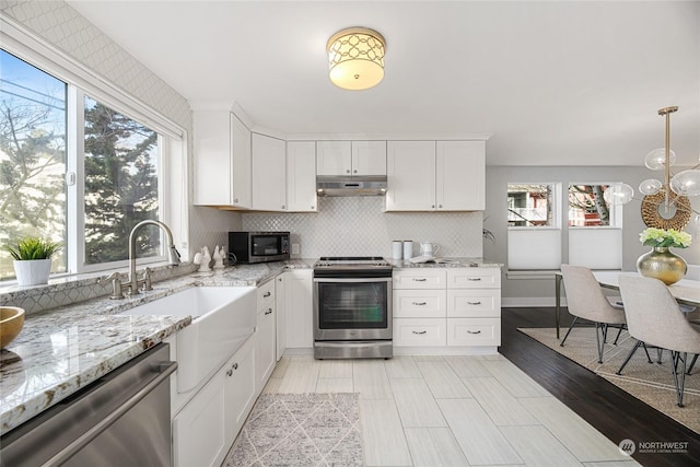 kitchen featuring white cabinetry, hanging light fixtures, stainless steel appliances, light stone counters, and a chandelier