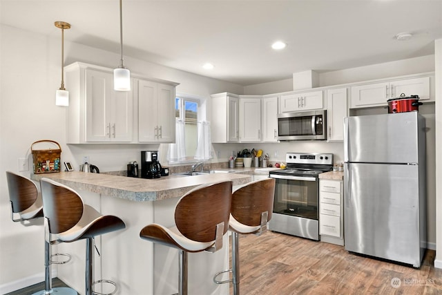 kitchen with appliances with stainless steel finishes, white cabinets, sink, kitchen peninsula, and pendant lighting