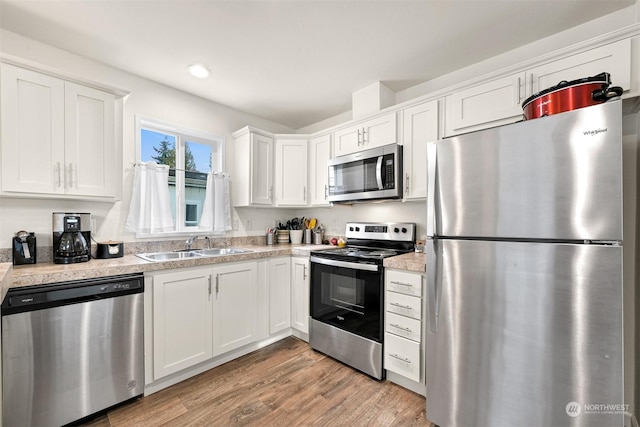 kitchen with sink, light wood-type flooring, white cabinetry, and appliances with stainless steel finishes