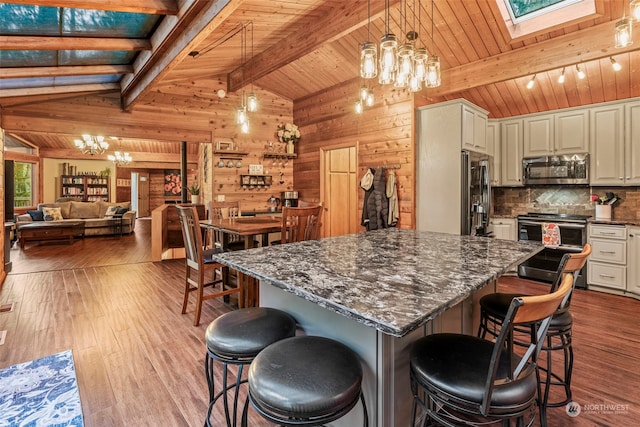 kitchen with light hardwood / wood-style flooring, appliances with stainless steel finishes, vaulted ceiling with skylight, a chandelier, and a breakfast bar area