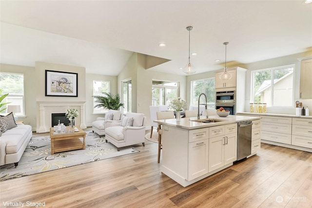 kitchen with sink, vaulted ceiling, a center island with sink, pendant lighting, and white cabinets