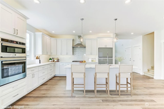 kitchen with pendant lighting, wall chimney range hood, white cabinetry, and appliances with stainless steel finishes