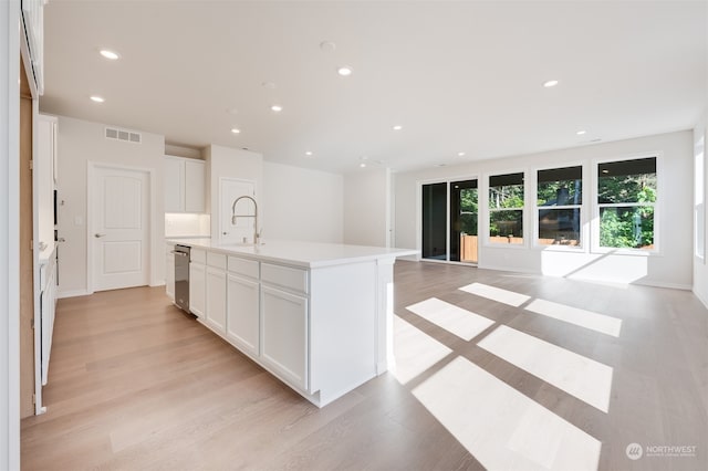 kitchen featuring sink, dishwasher, a kitchen island with sink, white cabinetry, and light wood-type flooring