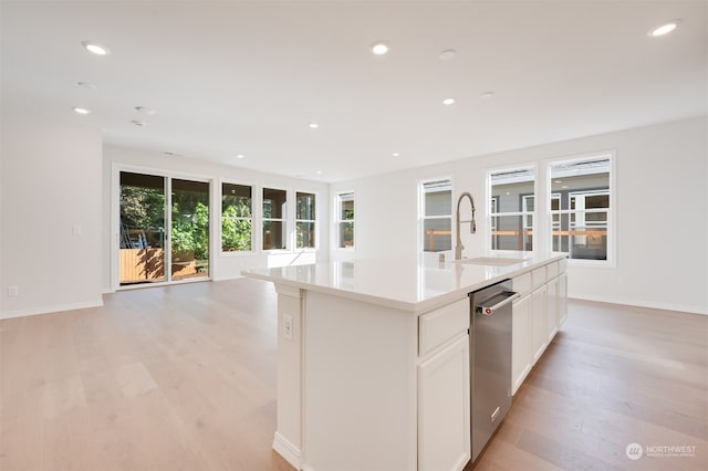 kitchen with sink, white cabinetry, light wood-type flooring, stainless steel dishwasher, and a kitchen island with sink