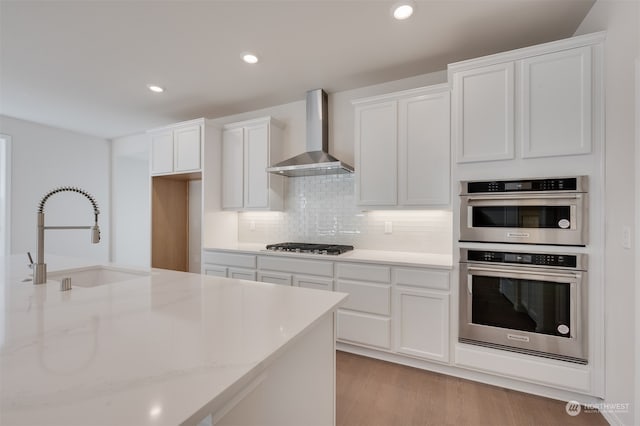 kitchen with sink, wall chimney range hood, white cabinets, and light stone counters