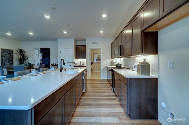 kitchen featuring sink, dark brown cabinets, light hardwood / wood-style flooring, a large island with sink, and appliances with stainless steel finishes