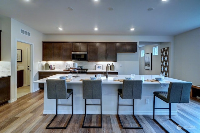 kitchen with sink, a breakfast bar area, a center island with sink, and light wood-type flooring