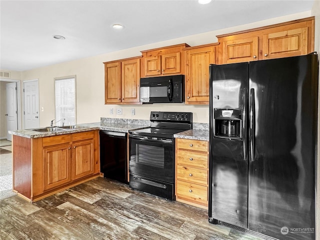 kitchen with sink, dark hardwood / wood-style floors, kitchen peninsula, light stone countertops, and black appliances